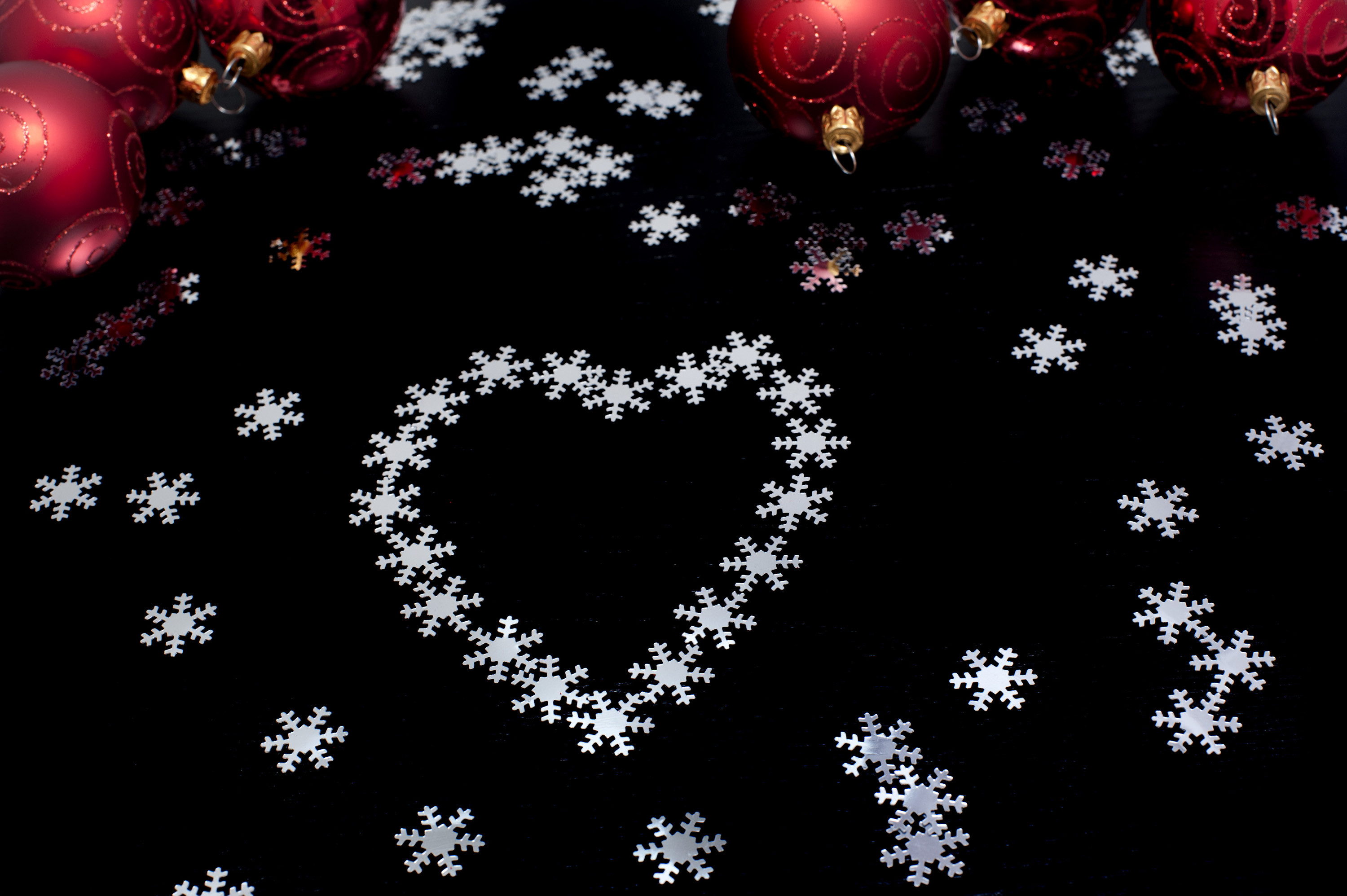 3000x1996 Christmas snowflake heart shape on a black background with scattered  snowflakes and colourful Christmas baubles
