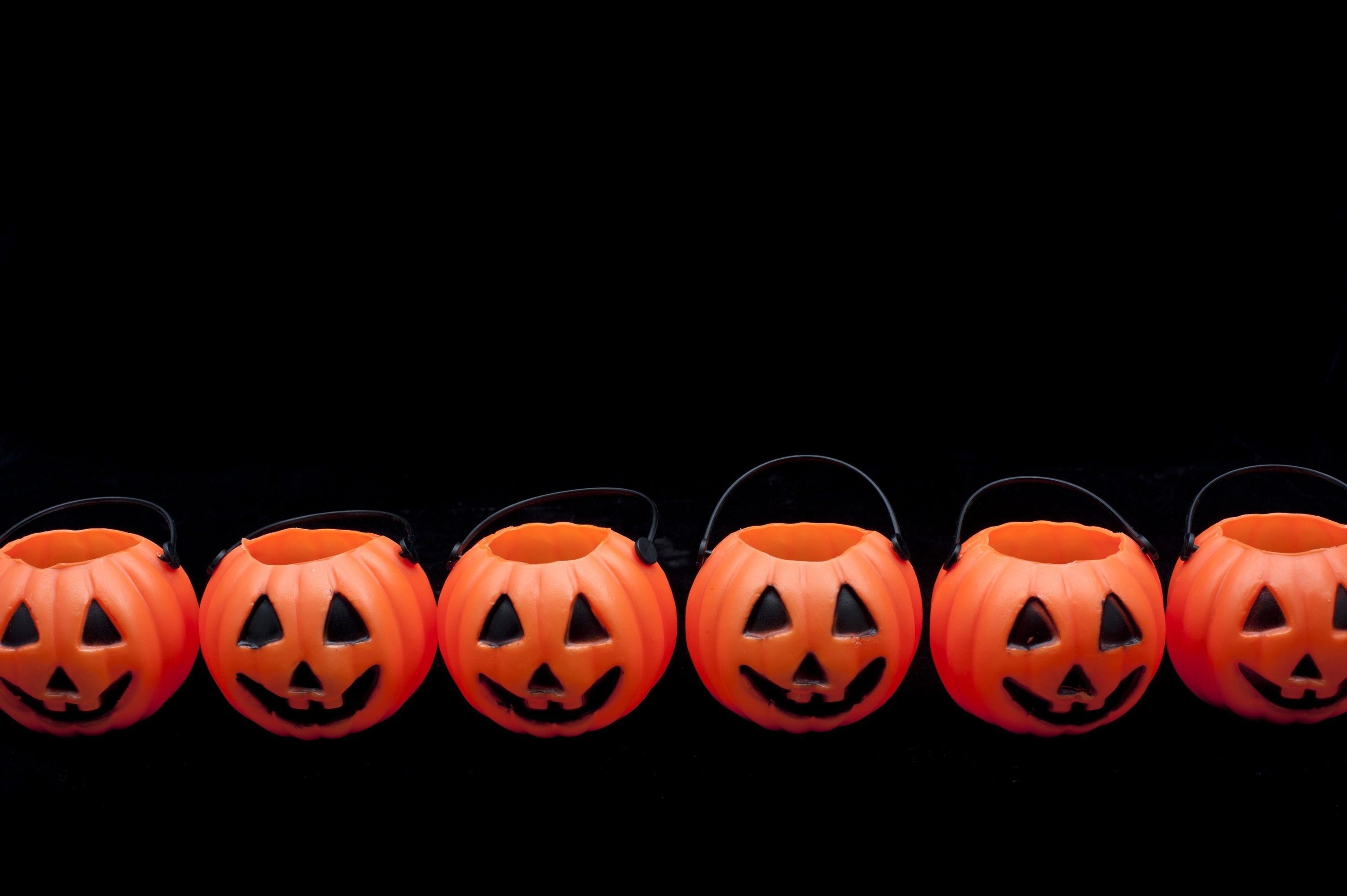 3000x1996 Row of orange ceramic Halloween pumpkin lantern ornaments on a dark  background forming a border with
