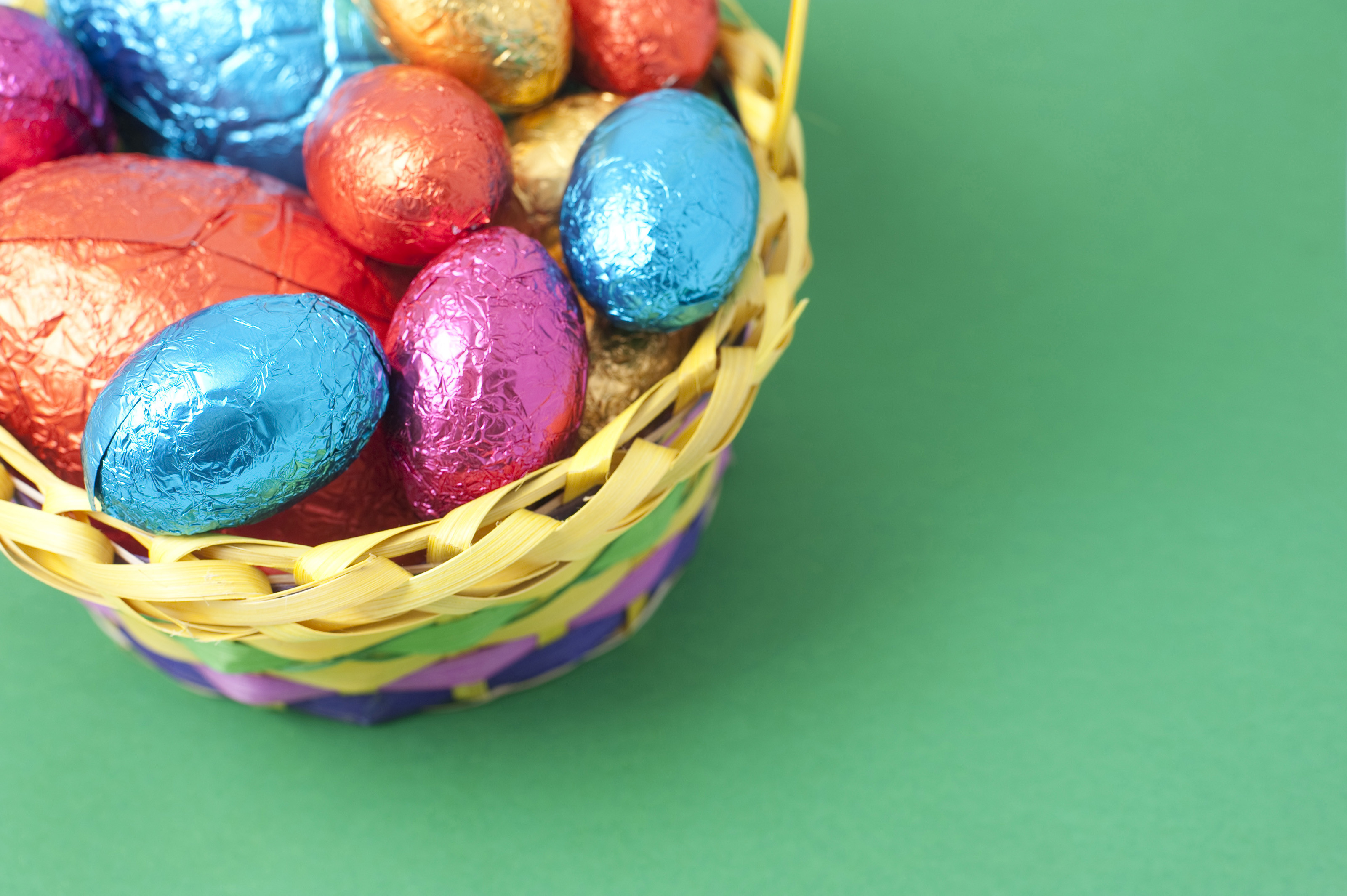 3200x2129 Easter Egg background with a basket filled with colourful foil wrapped eggs  in one corner and