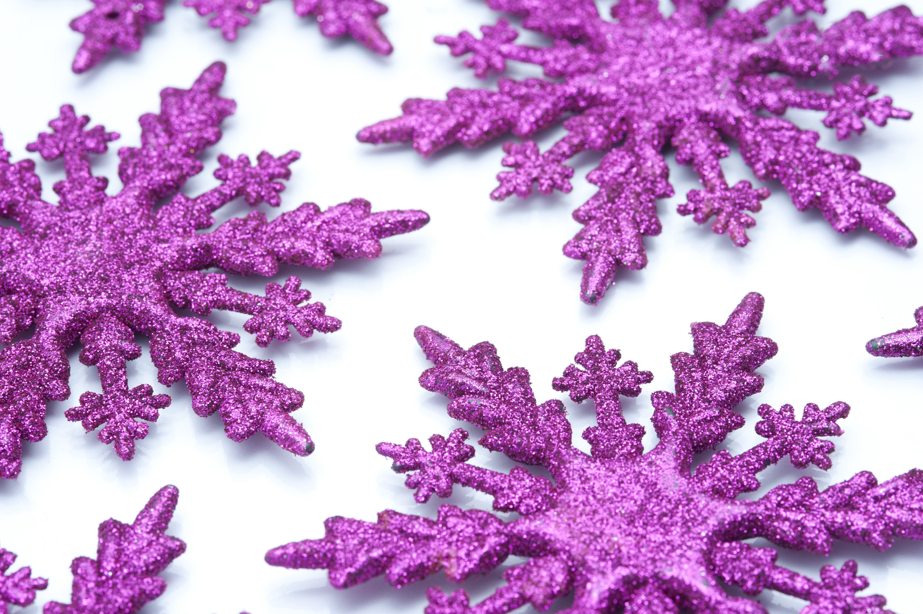 3000x1996 Pink snowflake ornaments with textured glitter surfaces scattered on a  white background to celebrate the festive