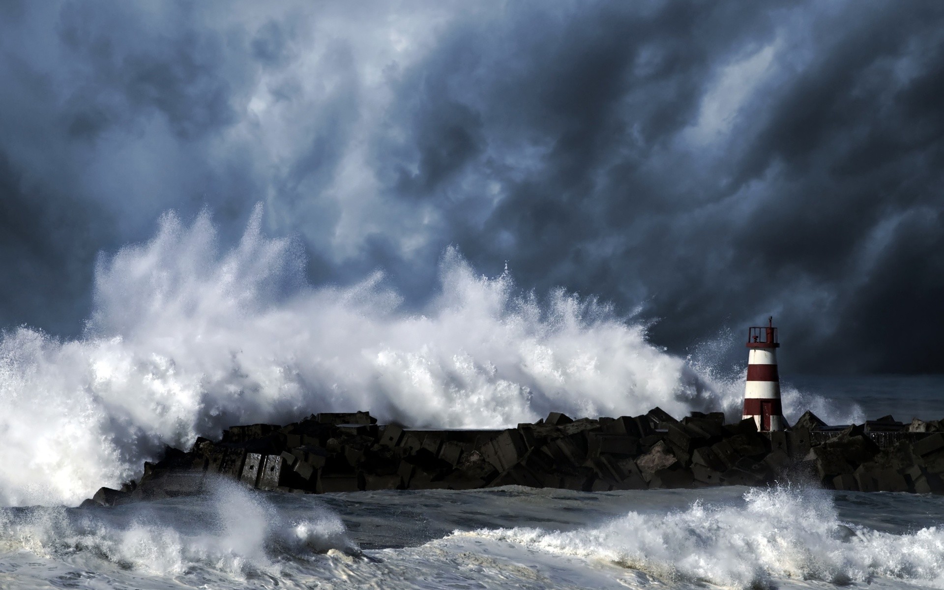 1920x1200 Light streaming over a stormy sea from a lighthouse on a rocky shore.  Description from